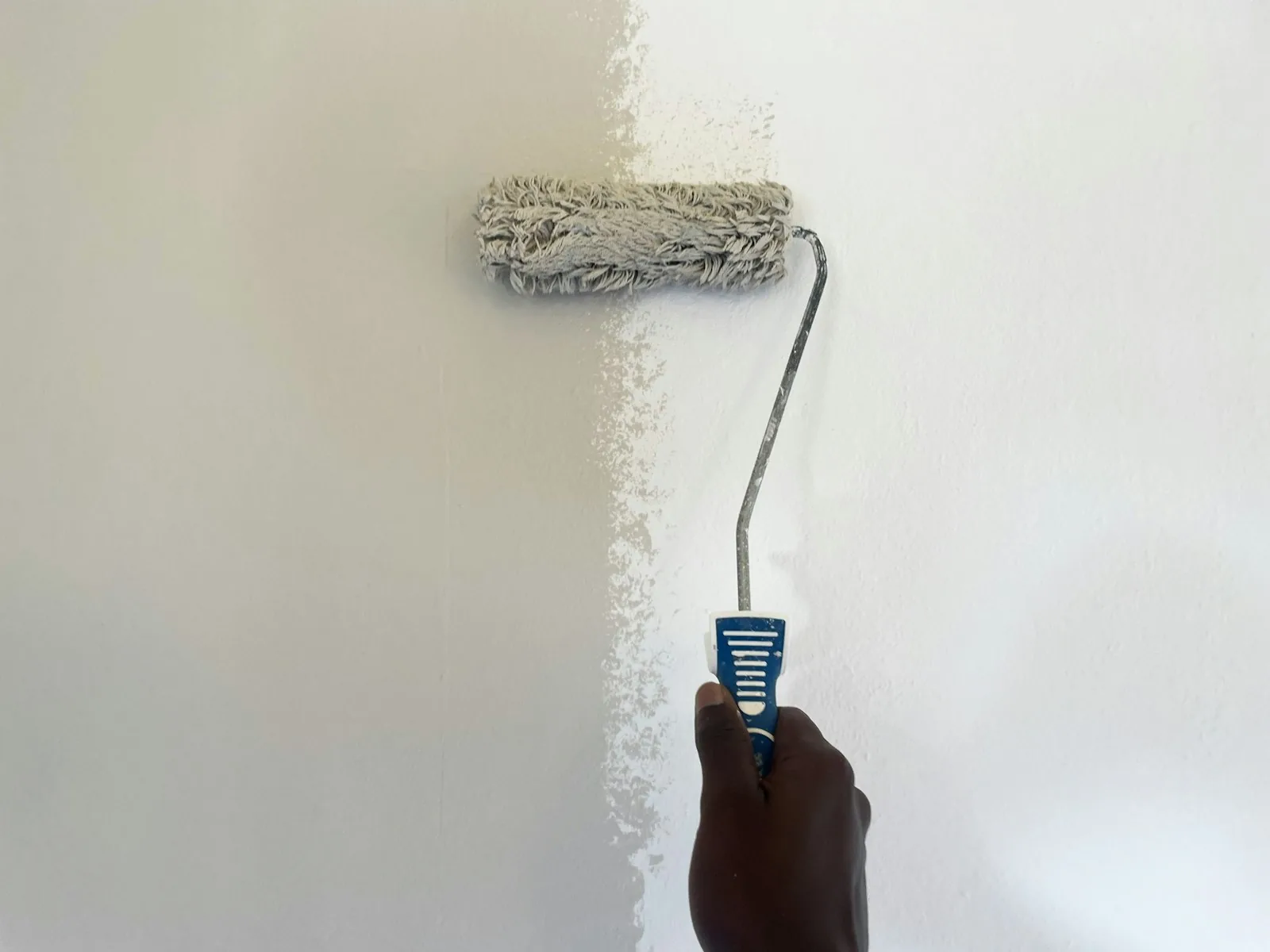 Paint roller covering a wall with fresh white paint