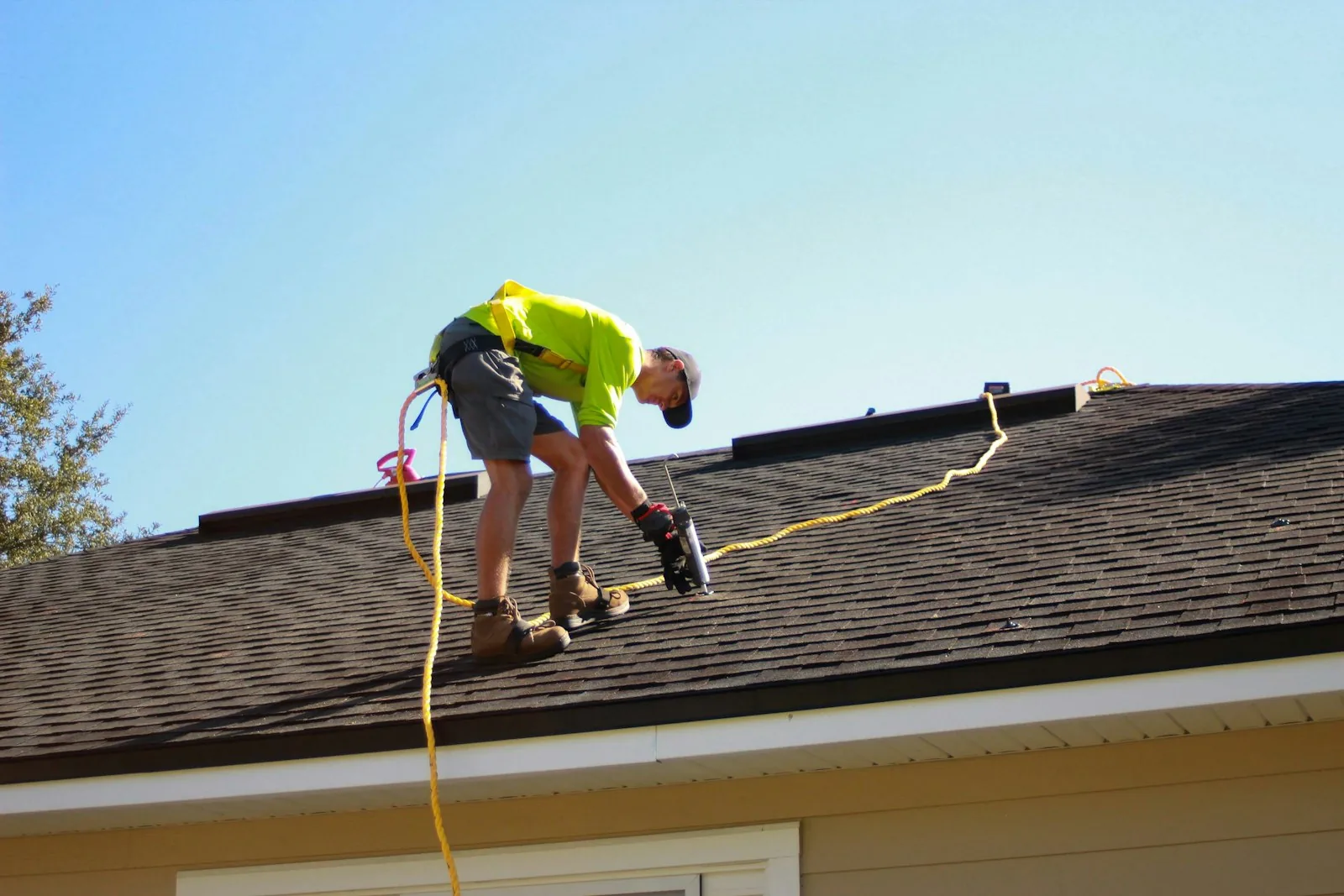 Roofer in a safety harness working on a shingle roof